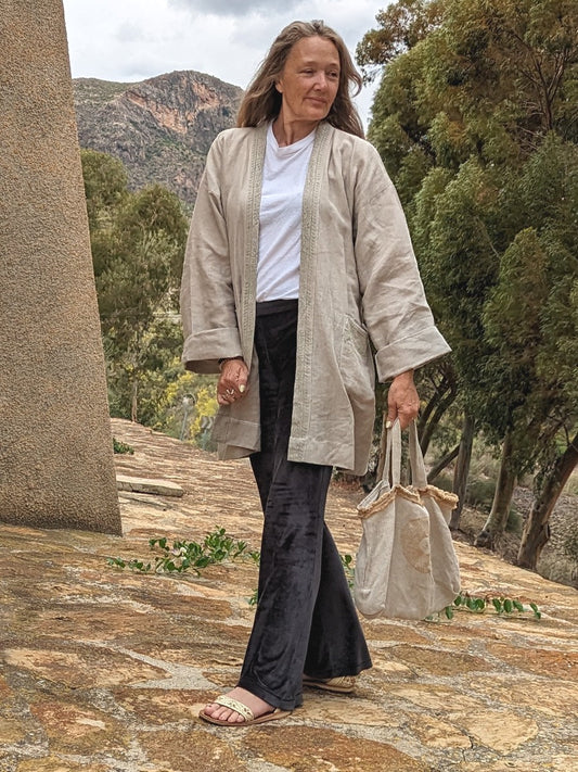 A person wearing a beige hemp kimono dress jacket with a belt, walking down stone stairs. They are also carrying a beige bag and wearing sneakers.
