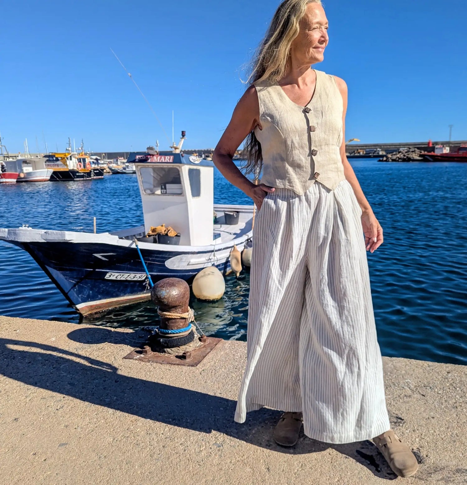 Beige linen sleeveless vest with button closures worn over wide-leg white and gray striped trousers
