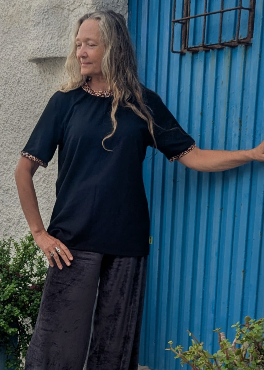 Woman in a black outfit standing against a blue corrugated metal wall.