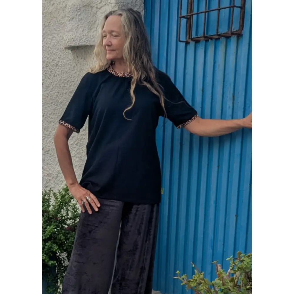 Woman in a black outfit standing against a blue corrugated metal wall.