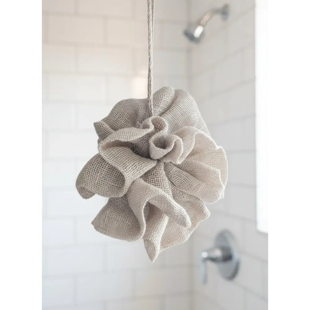 Beige bath pouf hanging on a hook with a plant in the background