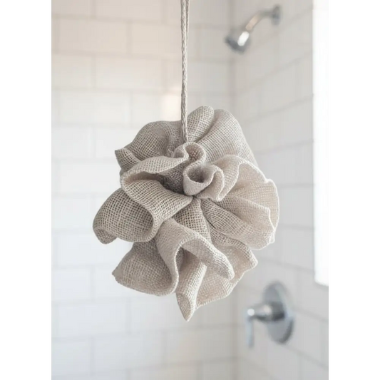 Beige bath pouf hanging on a hook with a plant in the background