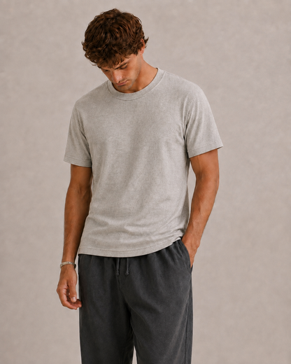 A man wearing a light stone pure Hemp t-shirt and dark gray drawstring pants, standing against a textured beige studio background. Hemp Horizon