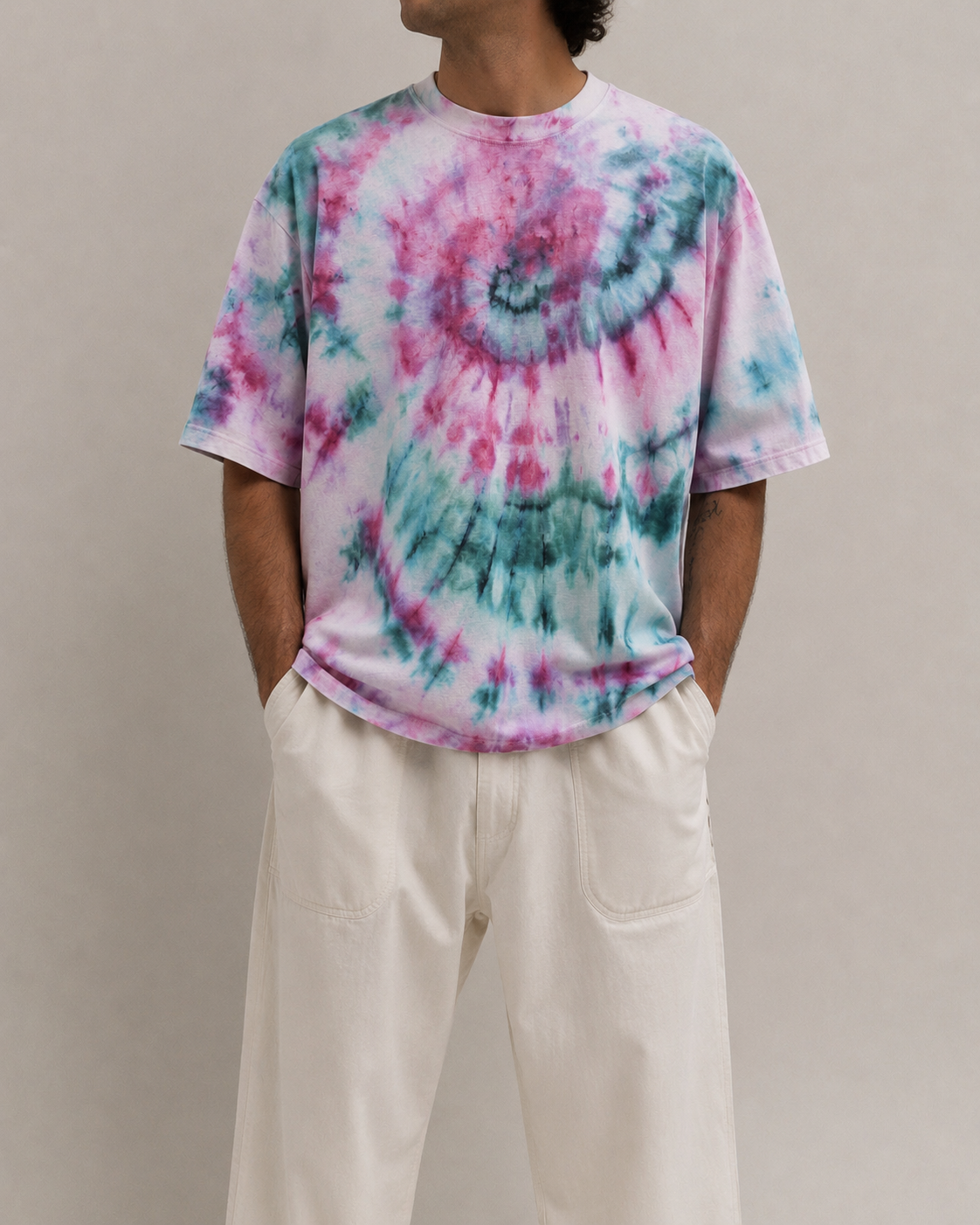 A person wearing a short-sleeve tie-dye t-shirt with  pink and teal swirls, paired with off-white wide-leg pants, against a hemp plain beige studio background. Hemp Horizon